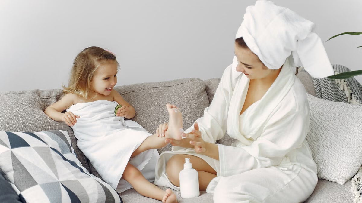 A mother and daughter enjoy bonding time on the sofa in cozy bathrobes, creating a warm family moment.